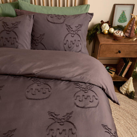 Chocolate brown duvet cover set with tufted Christmas pudding and holly motif, shown on a bed with matching pillowcases and a green cushion in a bedroom setting.