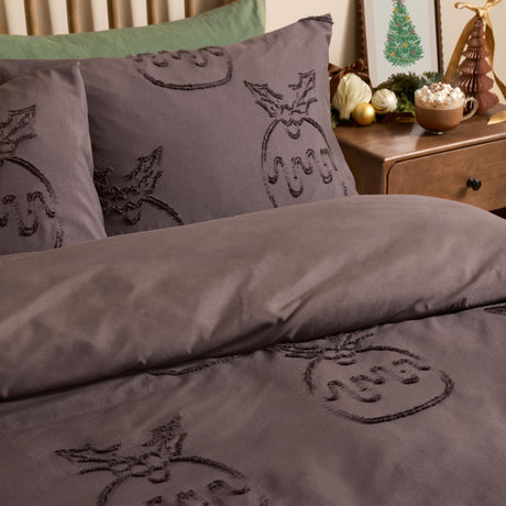 Chocolate brown duvet cover set with tufted Christmas pudding and holly motifs, shown on a bed with matching pillowcases in a bedroom setting.