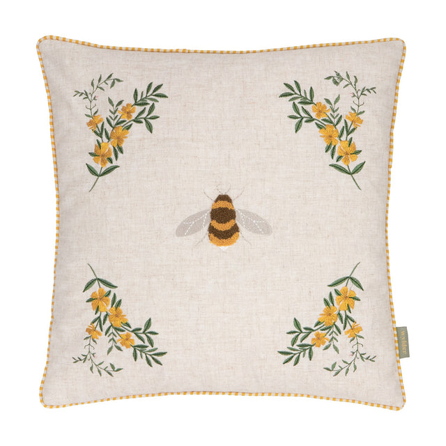 Square natural linen cushion with a tufted bee at the centre and embroidered yellow floral sprays in each corner, edged with yellow gingham piping, on a plain white background.
