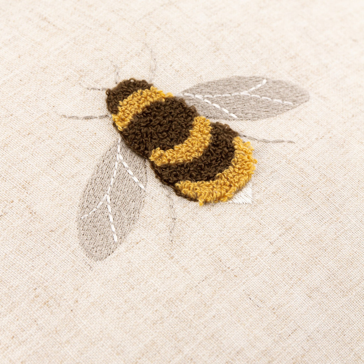 Close-up of the Rambbee Velvet Linen Cushion in Natural, showing a tufted bee in brown and gold loops with grey stitched wings on oatmeal linen.