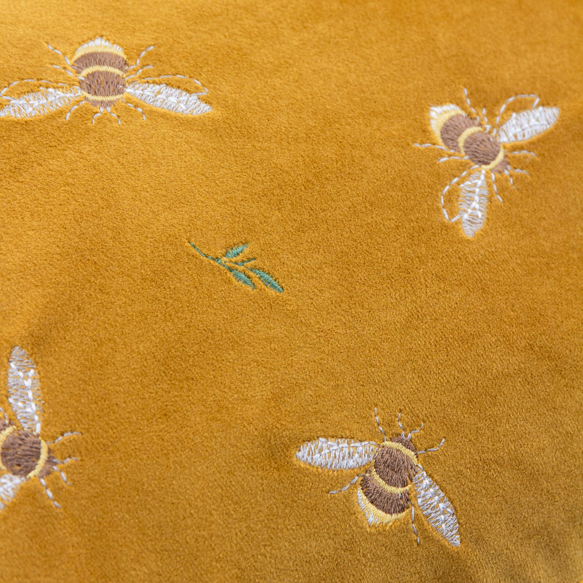 Close-up of the Rambbes Animal Velvet Cushion in honey gold, showing embroidered bees in cream, tan and yellow with small green leaf sprigs on velvet pile.