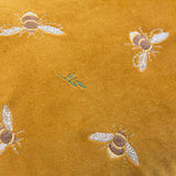 Close-up of the Rambbes Animal Velvet Cushion in honey gold, showing embroidered bees in cream, tan and yellow with small green leaf sprigs on velvet pile.