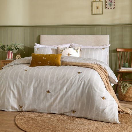 Ramble Cotton Striped Duvet Cover Set in natural, styled on a bedroom bed with embroidered bees, matching pillowcases, mustard velvet cushion and a woven throw.