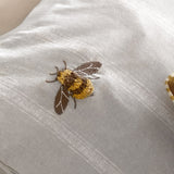 Close-up of the Ramble Cotton Striped Duvet Cover Set in natural, showing an embroidered, tufted bee in yellow, gold and brown thread on a subtle striped cotton ground.