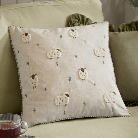 Rambshe Velvet Linen Cushion in Natural, a square cushion with tufted sheep and embroidered grass on a flecked linen-blend face, shown on a sofa with green cushions.