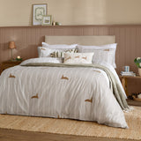Ramble Cotton Animal Duvet Cover Set in Sage on a bed, featuring embroidered hare motifs on a striped white and beige ground, styled with white pillowcases and a green throw.