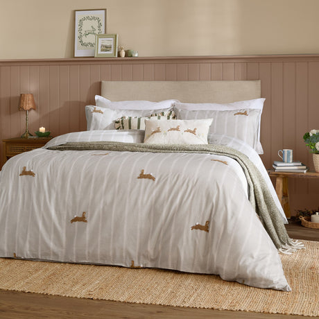 Ramble Cotton Animal Duvet Cover Set in Sage on a bed, featuring embroidered hare motifs on a striped white and beige ground, styled with white pillowcases and a green throw.