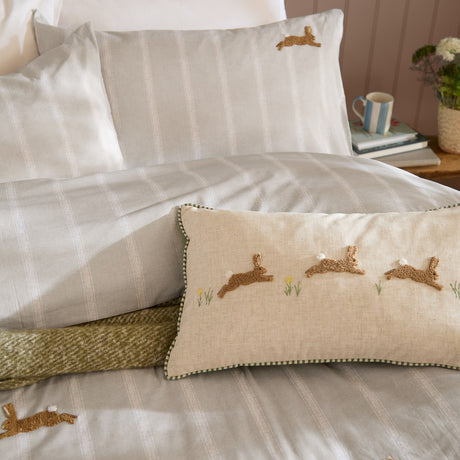 Sage Ramble Cotton Animal Duvet Cover Set on a bed with striped hare-embroidered pillowcases, a matching three-hare cushion, and a green woven throw.