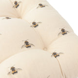 Close-up of the Rbumbbe Linen Cotton Seat Pad in natural cotton, showing tufted buttoned dimples and a hand-painted bumble bee print across the slub-textured fabric.