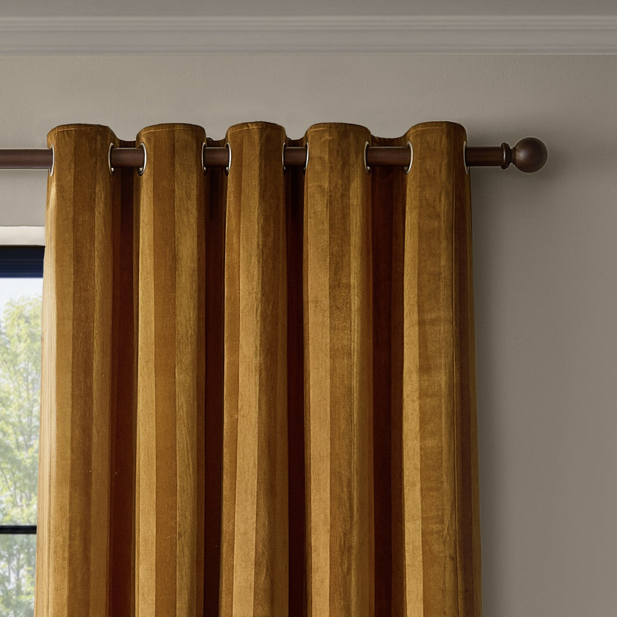 Regency Stripe Velvet Eyelet Curtains in antique gold, fully lined, shown with eyelet heading on a dark metal pole against a neutral wall near a window.