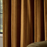 Regency Stripe Velvet Fully Lined Eyelet Curtains in antique gold, shown in deep, light-catching folds beside a window, with an olive sofa edge visible in the room.