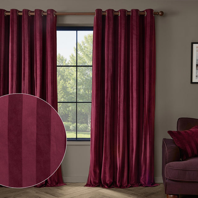 Regency Stripe Velvet Fully Lined Eyelet Curtains in burgundy, hung on a wooden pole beside a window in a living room, with a fabric close-up inset showing the self-stripe velvet texture.