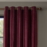 Regency Stripe Velvet Fully Lined Eyelet Curtains in burgundy, self-striped velvet fabric with grommet top hanging from a wooden pole against a beige wall.