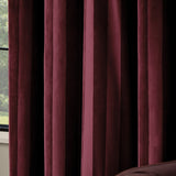 Close-up of Regency Stripe velvet eyelet curtains in burgundy, showing deep folds with a subtle self-stripe catching light across the pile, beside a window.