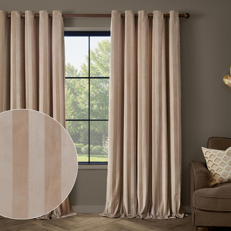 Regency Stripe Velvet Fully Lined Eyelet Curtains in beige with subtle self-stripe pile, shown hanging on a wooden rod beside a window in a living room setting.