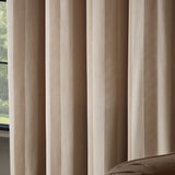 Regency Stripe fully lined eyelet curtains in beige velvet with a subtle self-stripe pile, shown floor-to-ceiling beside a window in a living room setting.