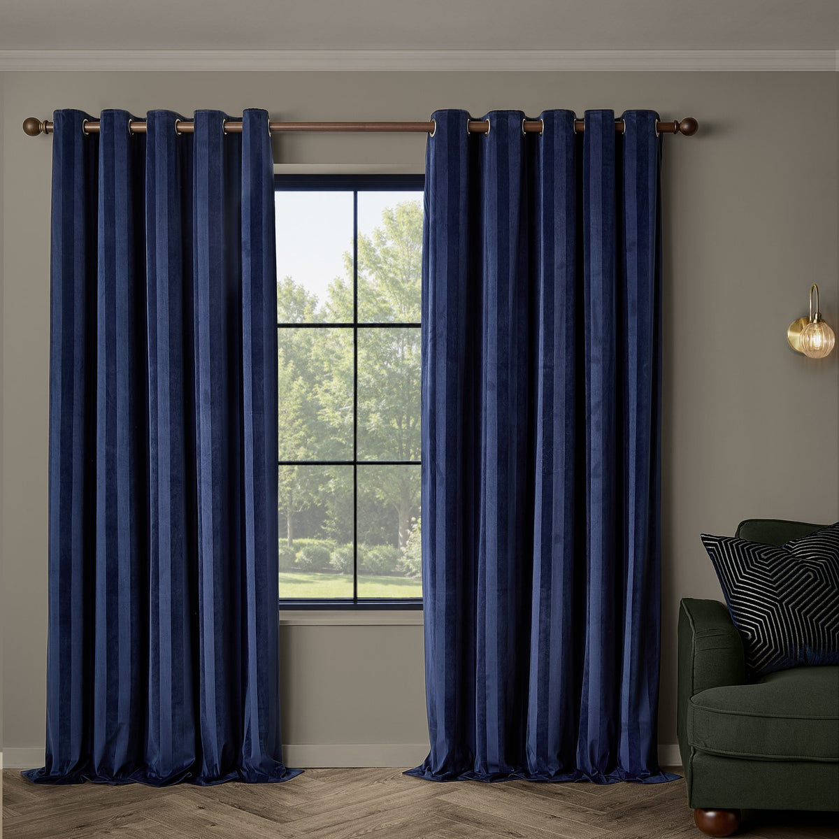 Regency Stripe velvet eyelet curtains in Midnight navy, fully lined with grommet top, hung either side of a window in a living room with a dark green sofa.