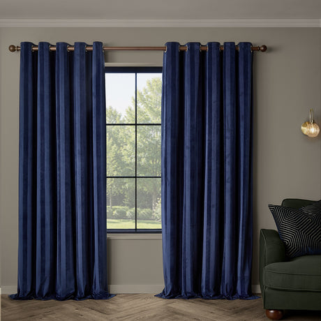 Regency Stripe velvet eyelet curtains in Midnight navy, fully lined with grommet top, hung either side of a window in a living room with a dark green sofa.