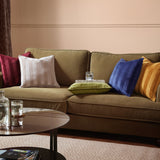 Olive green velvet cushion with woven vertical stripe jacquard pattern, styled on a green sofa alongside burgundy, cream, blue and mustard cushions.