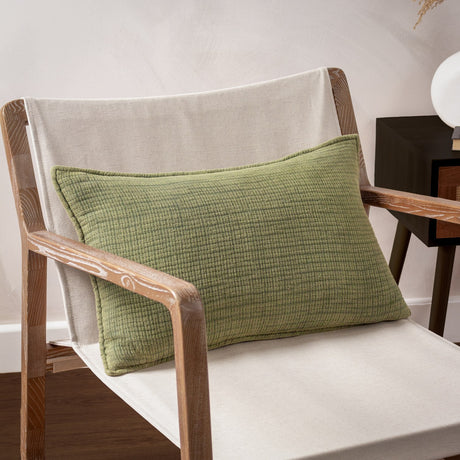 Ribble reversible cotton cushion in khaki, lumbar-shaped with a ribbed, stonewashed texture, shown propped on a wooden armchair against a neutral wall.