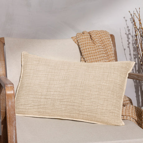 Ribble Reversible Cotton Cushion in natural with a textured ribbed weave, shown on a wooden armchair beside a woven throw and dried branches.