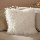 Rowan Faux Fur Plain Velvet Cushion in ecru, square scatter cushion with shaggy long-pile front, shown on a beige sofa in a living room setting.