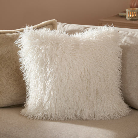 Rowan Faux Fur Plain Velvet Cushion in ecru, square scatter cushion with shaggy long-pile front, shown on a beige sofa in a living room setting.