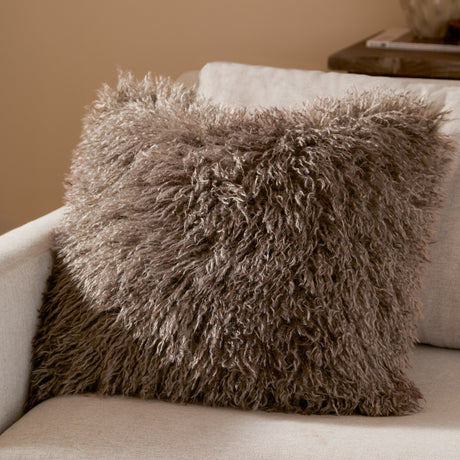 Rowan Faux Fur Cushion in mocha brown with shaggy Mongolian-style pile, shown square on a cream armchair in a living room setting.