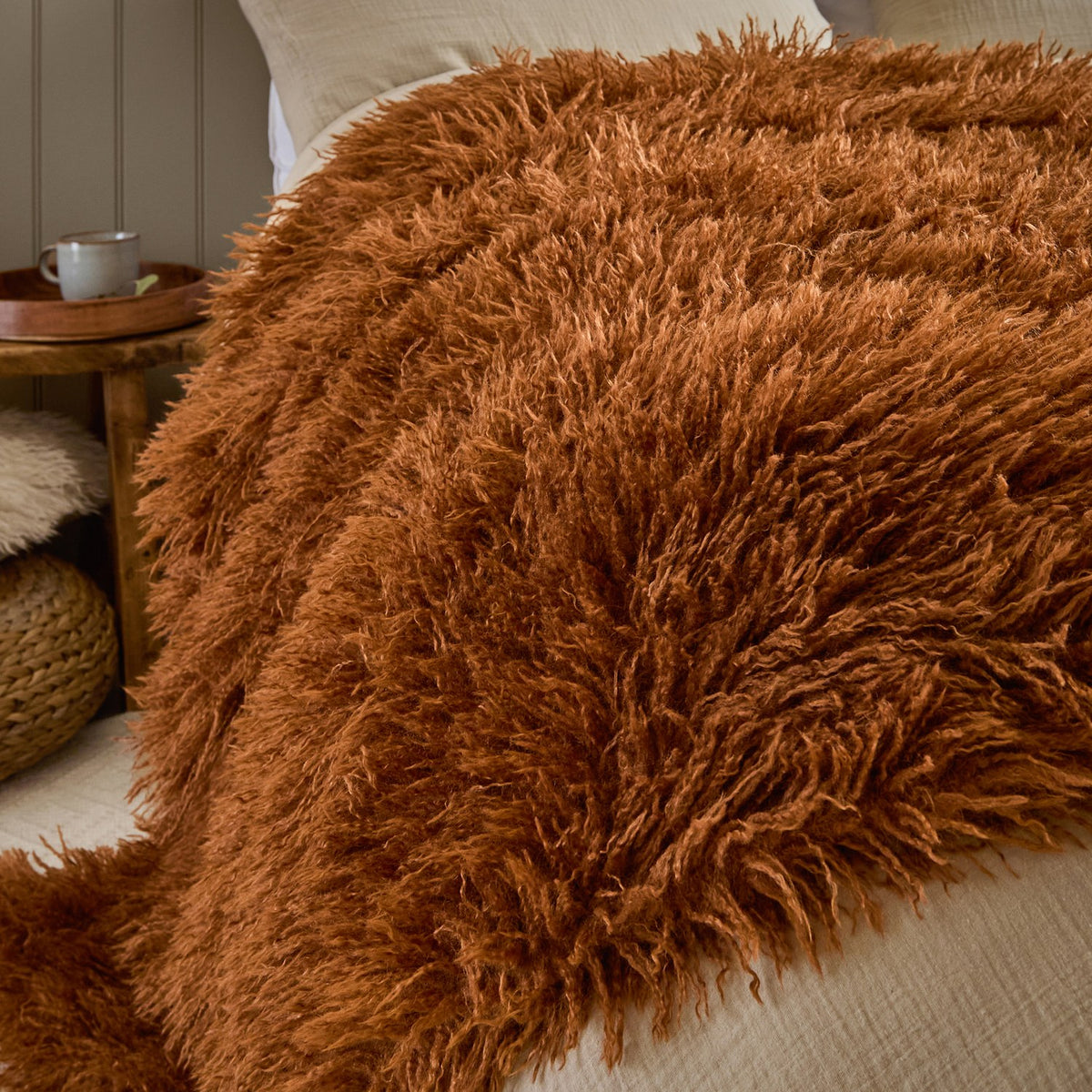 Rowan Faux Fur Plain Velvet Throw in ginger, shaggy long-pile fur texture draped over a bed with neutral linen bedding in a bedroom setting.