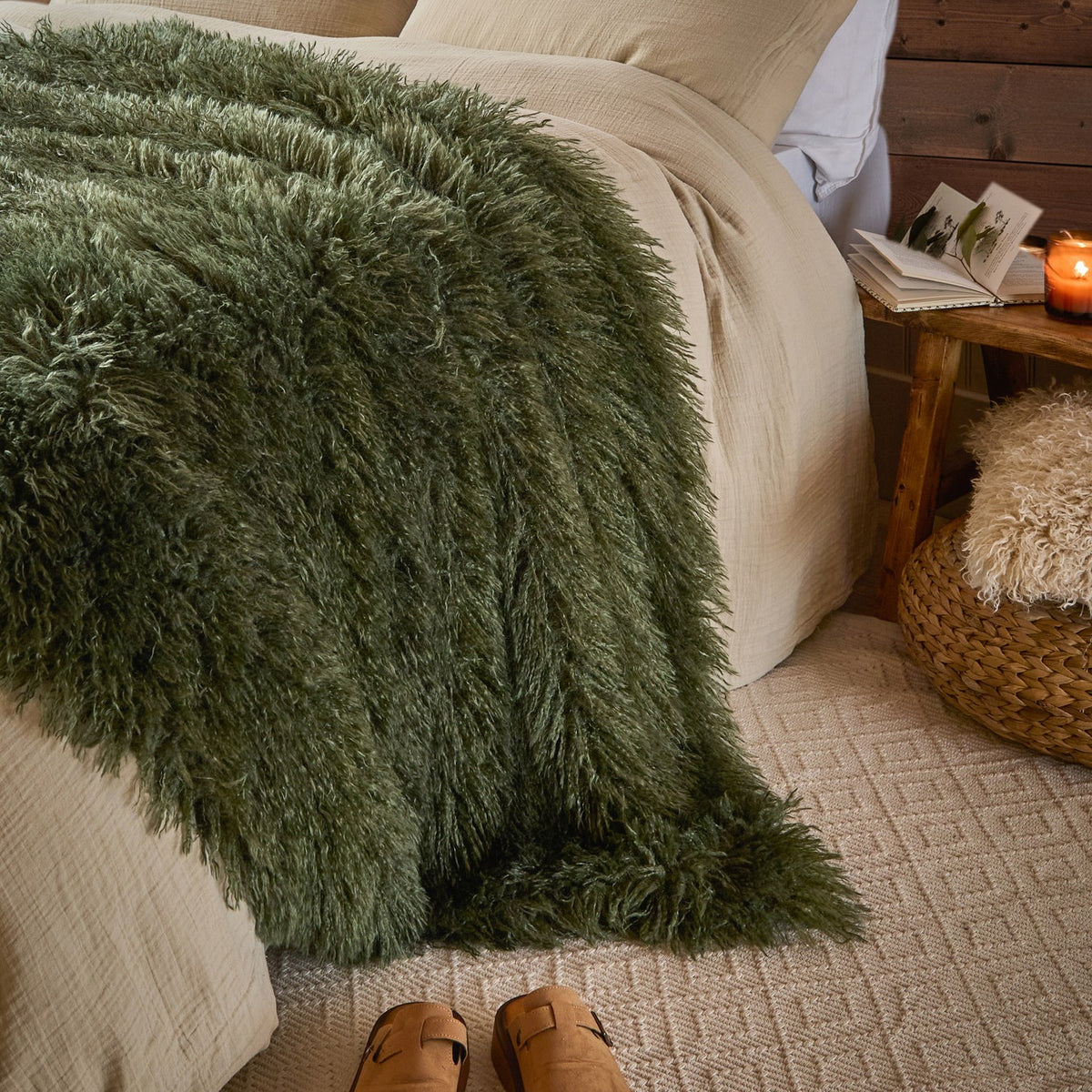 Rowan Faux Fur Plain Velvet Throw in khaki draped over a bed with shaggy fur texture, styled in a bedroom with cream bedding and a wooden bedside table.