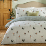 Robins Return cotton duvet cover set in cream with a robin and fir tree print, styled on a bed with matching pillowcases and a reversible green striped edge, in a bedroom setting.