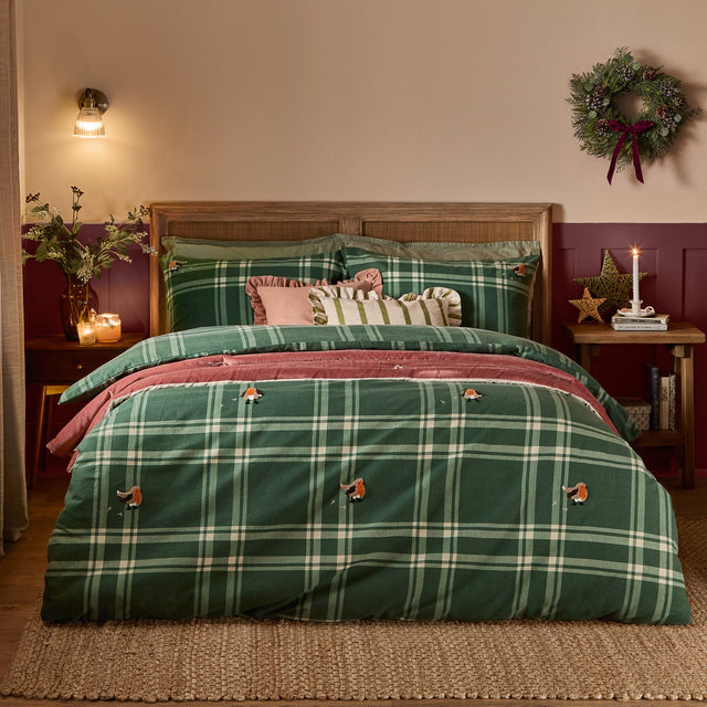 Ramble Cotton Check Duvet Cover Set in green plaid with embroidered robin motifs, styled on a bed with pink cushions in a rustic bedroom setting.