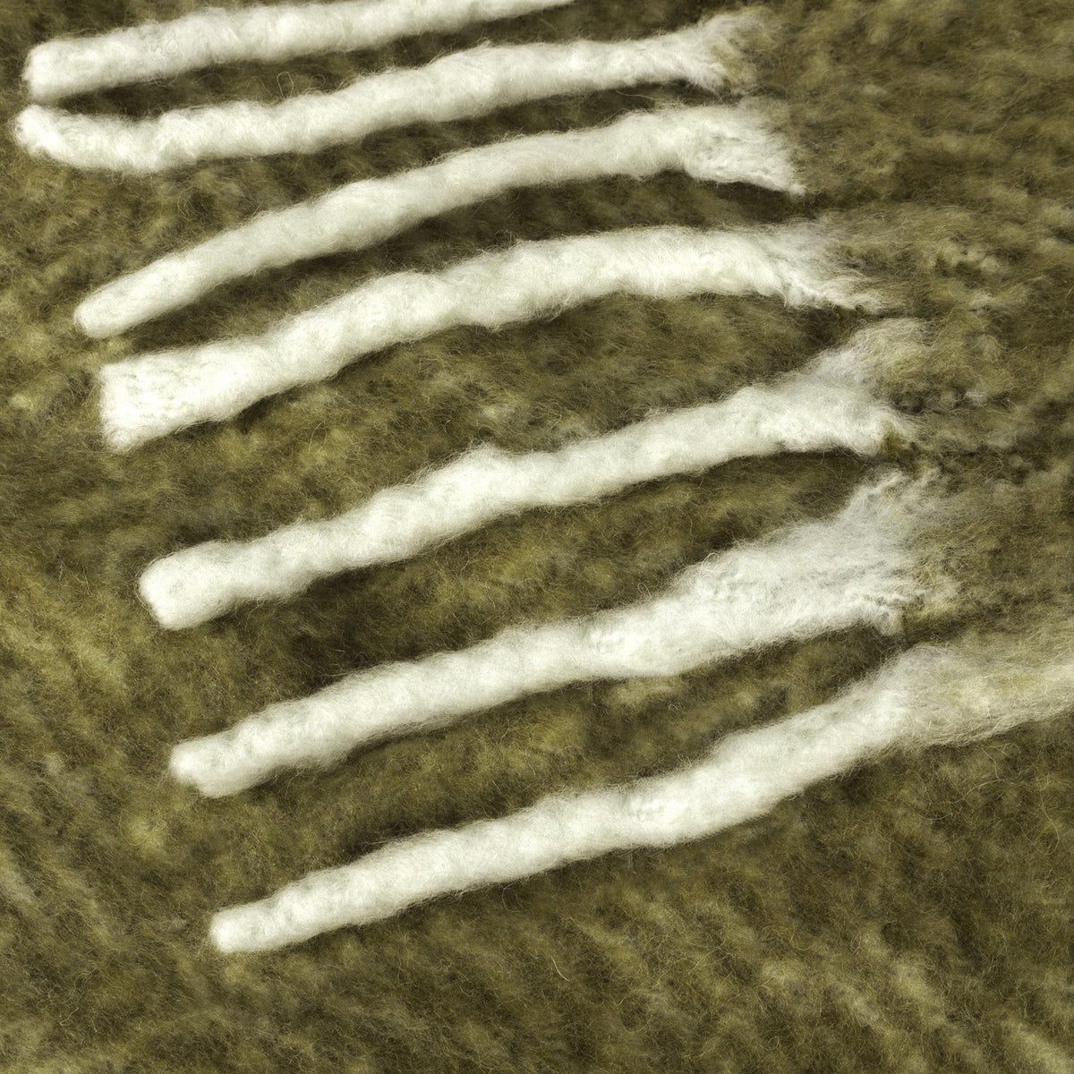 Close-up of the Rawton Ombre Herringbone Wool Throw in Natural/Moss, showing moss-green herringbone weave with cream fringe tassels at the edge.