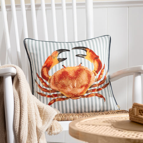 Salcombe Crab velvet cushion in orange and rust tones on a grey-blue and white striped ground, shown on a white rocking chair with a knitted throw.