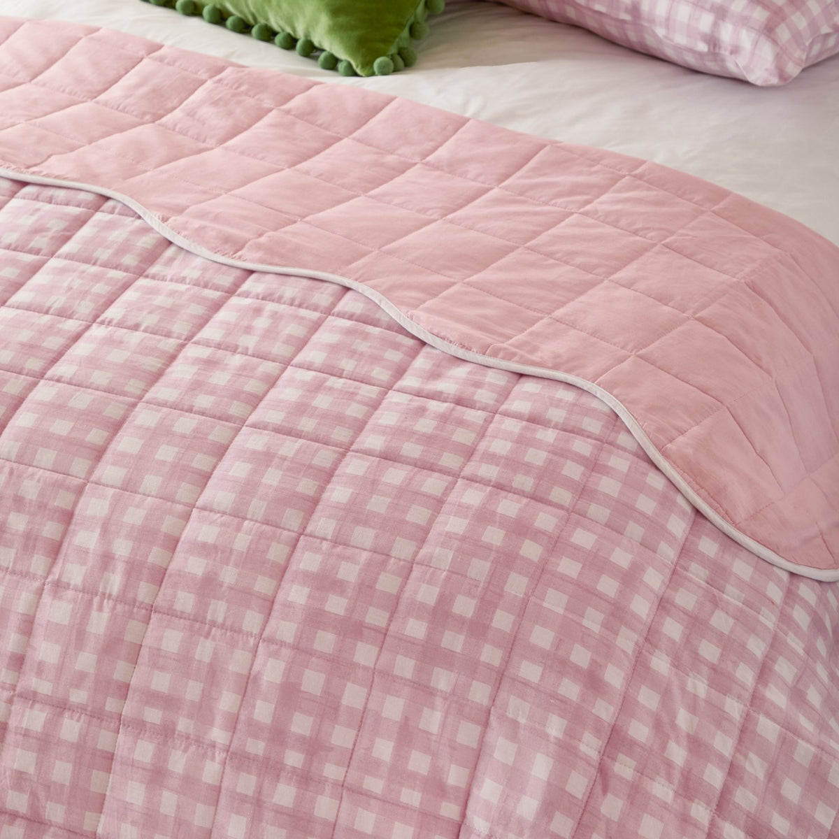 Scallop Plain Cotton Blend Bedspread on a bed, showing pink and white gingham check reverse with a scalloped white-trimmed pink quilted top edge.