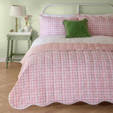 Pink square-quilted cotton blend bedspread with scalloped white-trimmed edge and matching pillow shams, styled with a green cushion in a light green bedroom.