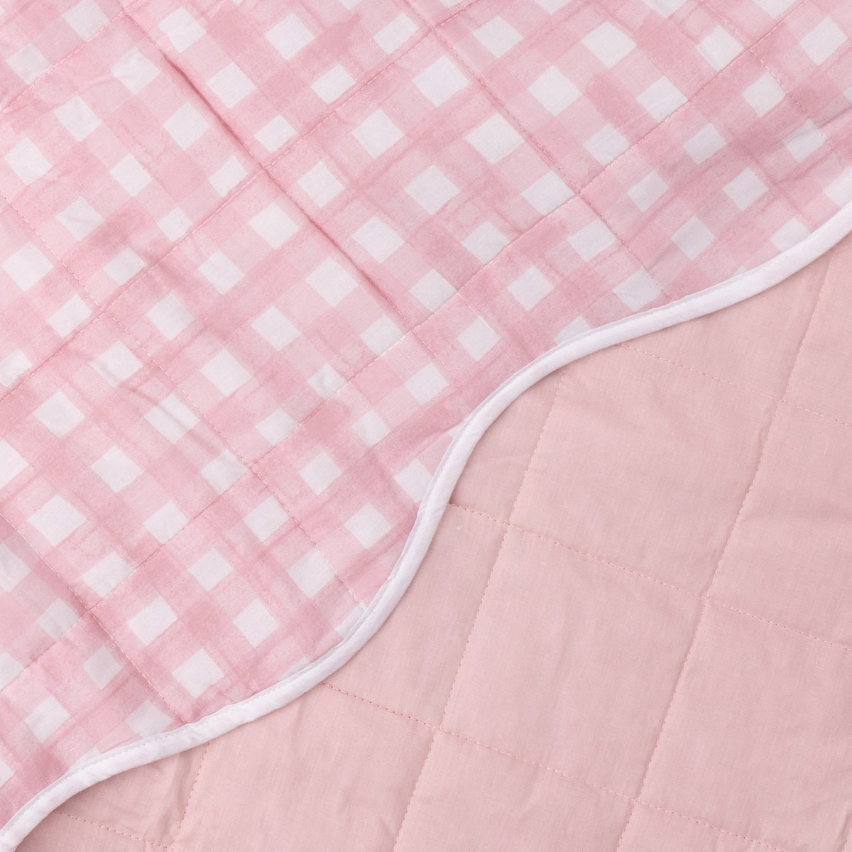 Close-up of the reversible Scallop Plain Cotton Blend Bedspread in pink, showing square quilting with pink gingham check on one side and plain pink on the other, edged in white.