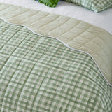 Reversible Scallop quilted bedspread on a bed, showing sage green gingham check on one side and plain sage green on the other with a white scalloped trim.