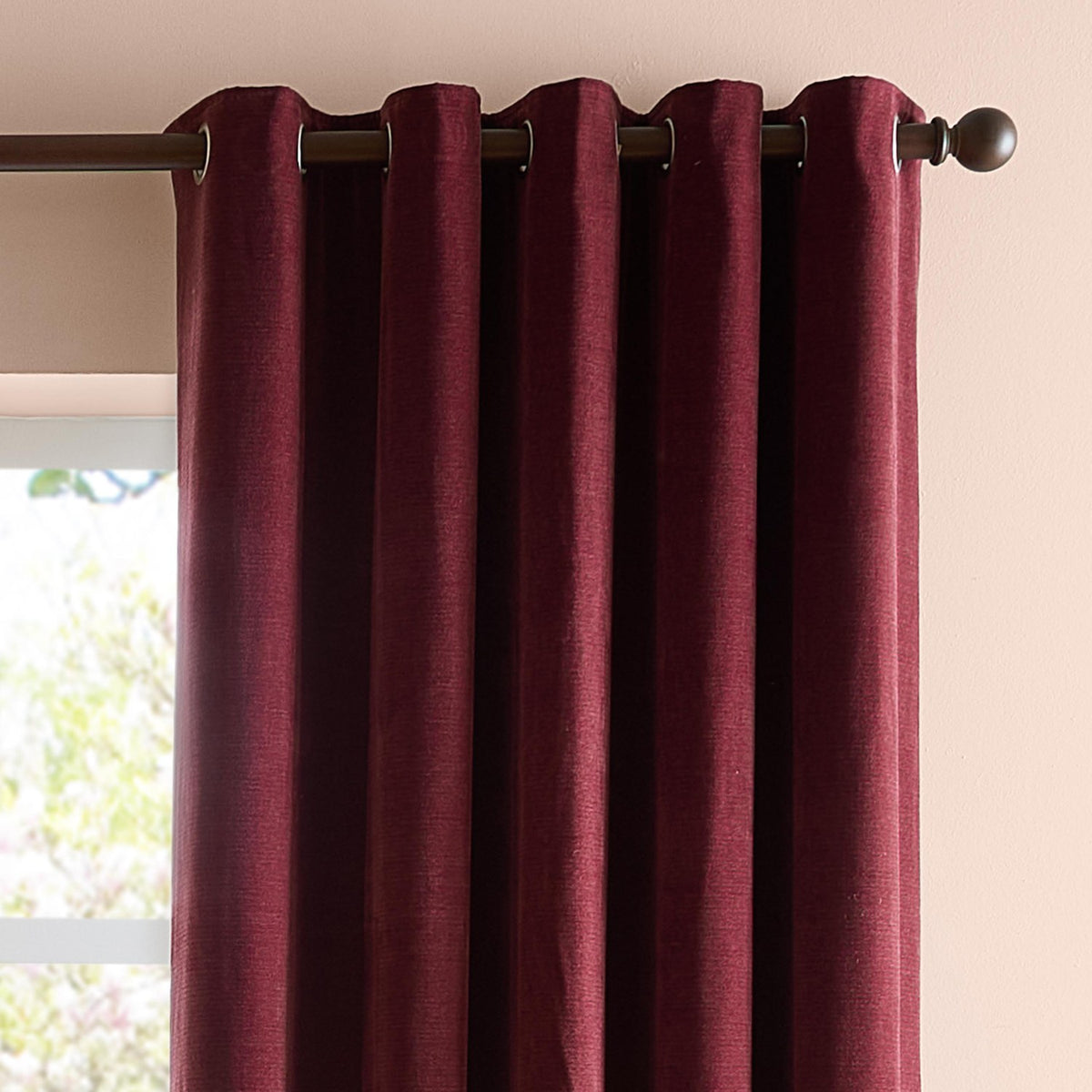 Soft Chenille Plain Lined Eyelet Curtains in deep beetroot red, hung on a dark pole with metal eyelets, showing folded fabric texture near a window.