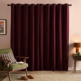 Soft chenille eyelet curtains in beetroot red hanging in even folds from a dark pole, shown in a living room with a green armchair and pink wall.