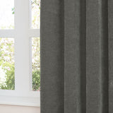 Charcoal grey chenille eyelet curtain in soft folds by a white-framed window, showing dense matt-textured fabric with a garden view beyond.