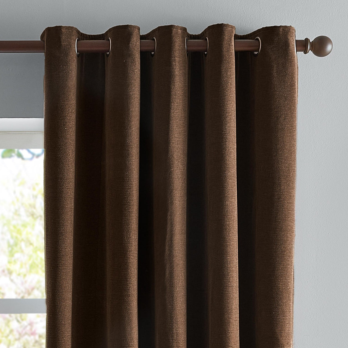Chocolate brown chenille eyelet curtains hanging on a dark metal pole, showing grommet header and textured woven fabric against a light grey wall.