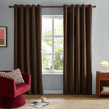 Chocolate brown chenille eyelet curtains hanging on a rod either side of a window in a living room, styled with a red armchair and wooden side table.