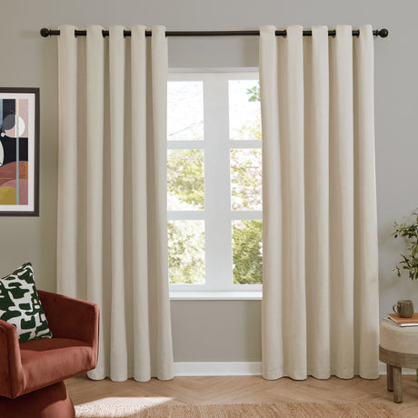 Ecru chenille eyelet curtains hung on a dark rod either side of a window in a living room, shown with a rust armchair and patterned cushion.
