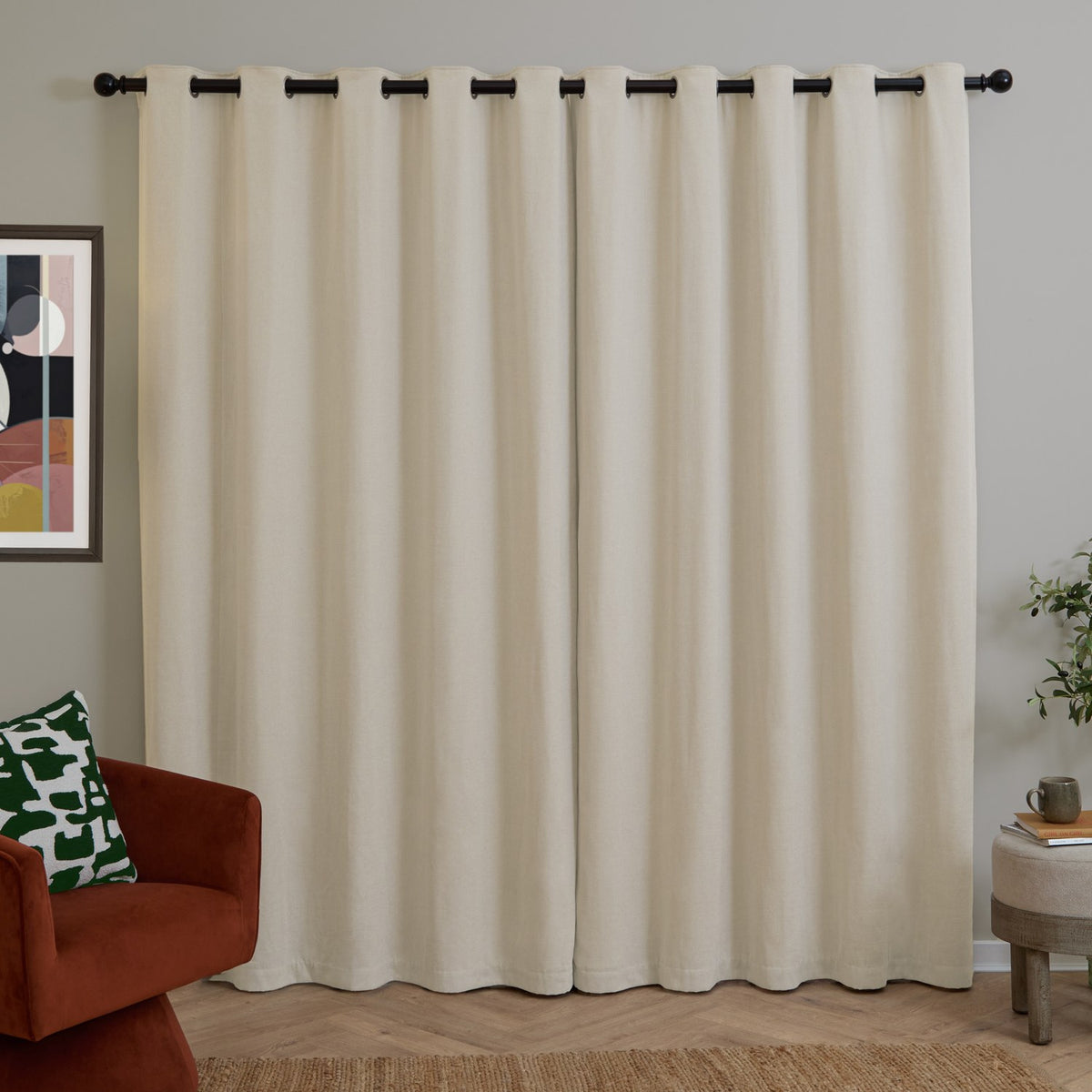 Ecru chenille eyelet curtains with dark grommets on a black rod, shown as a pair in a living room with a rust armchair and gallery-framed art.