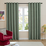 Green chenille eyelet curtains with grommet header hung on a black rod, shown in a living room beside a window, red armchair, and framed art.
