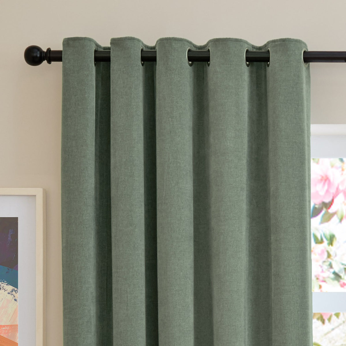 Green chenille eyelet curtains with silver grommets on a black rod, shown in soft folds against a neutral wall near a framed print.