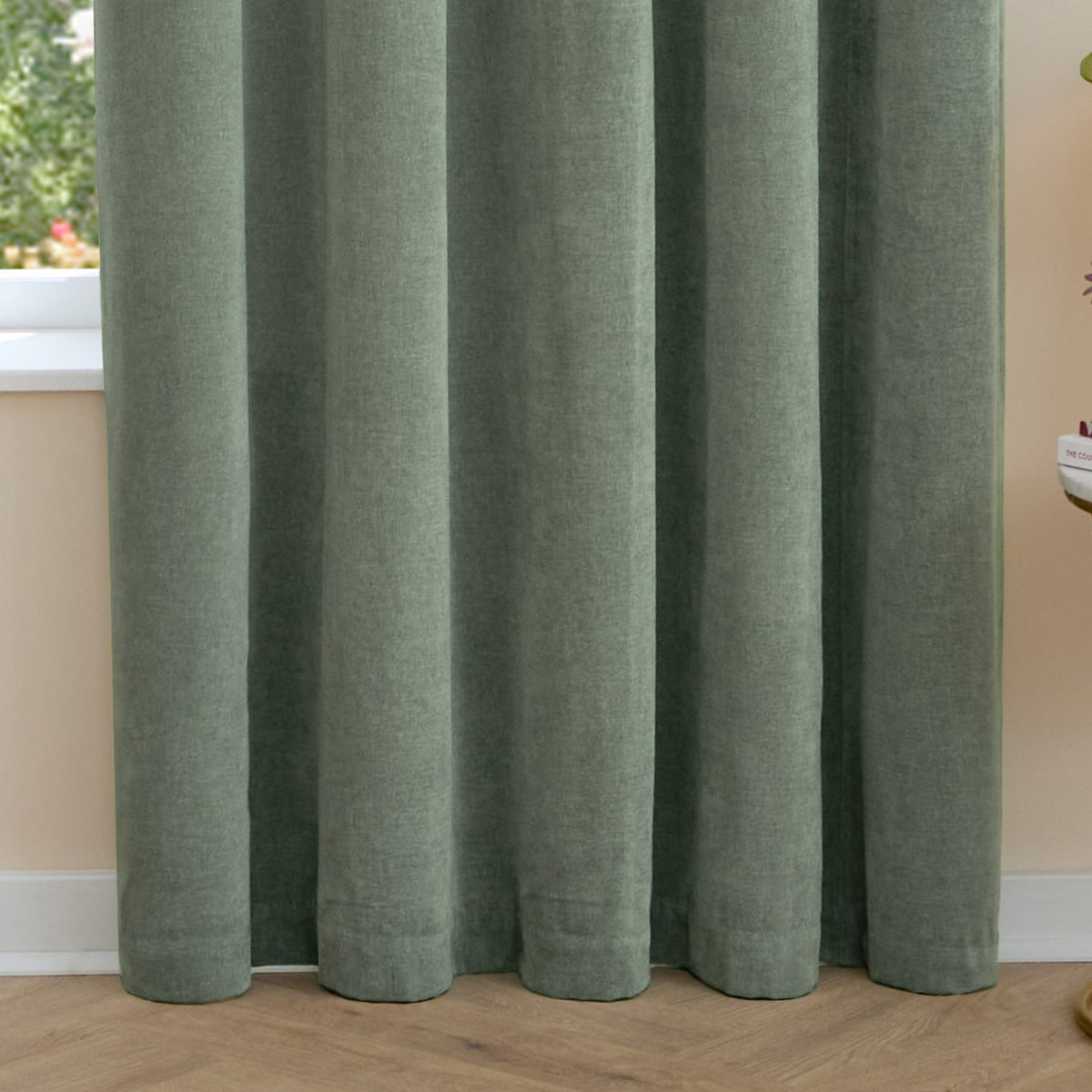Close-up of Soft Chenille Plain Lined Eyelet Curtains in green, showing soft matt fabric folds hanging by a window with wooden flooring.