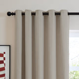 Natural oatmeal chenille eyelet curtain with metal grommets on a black rod, shown against a light wall beside a window in a living space.