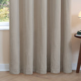 Natural oatmeal chenille eyelet curtains hanging in soft folds by a window, shown in a living room setting with wood flooring and a side table.